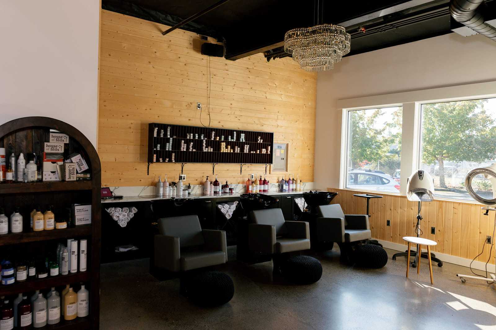 Modern salon interior with styling chairs, wood accents, large windows, and hair products displayed.