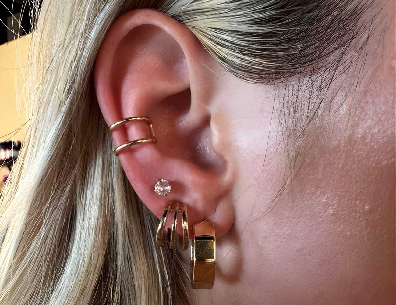 Close-up of an ear with four gold earrings and a small diamond stud.