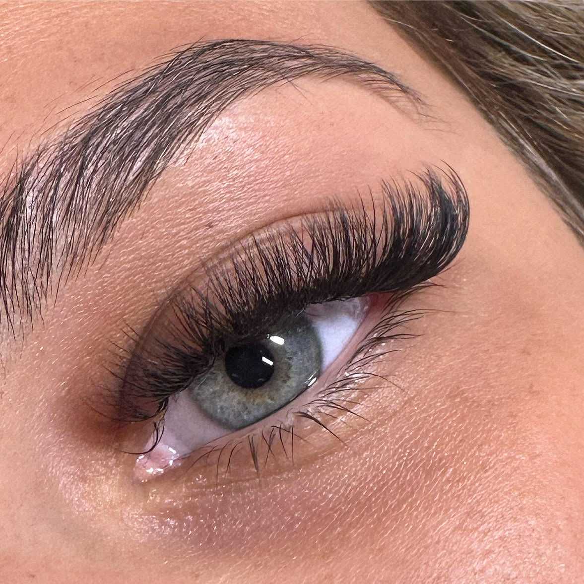 Close-up image of a woman's eye with lush, full lashes fanning outwards to display Salon Kathleen's high-quality lash extension options. Long, dark lashes uniformly coat the upper lash line for a thick, voluminous look.