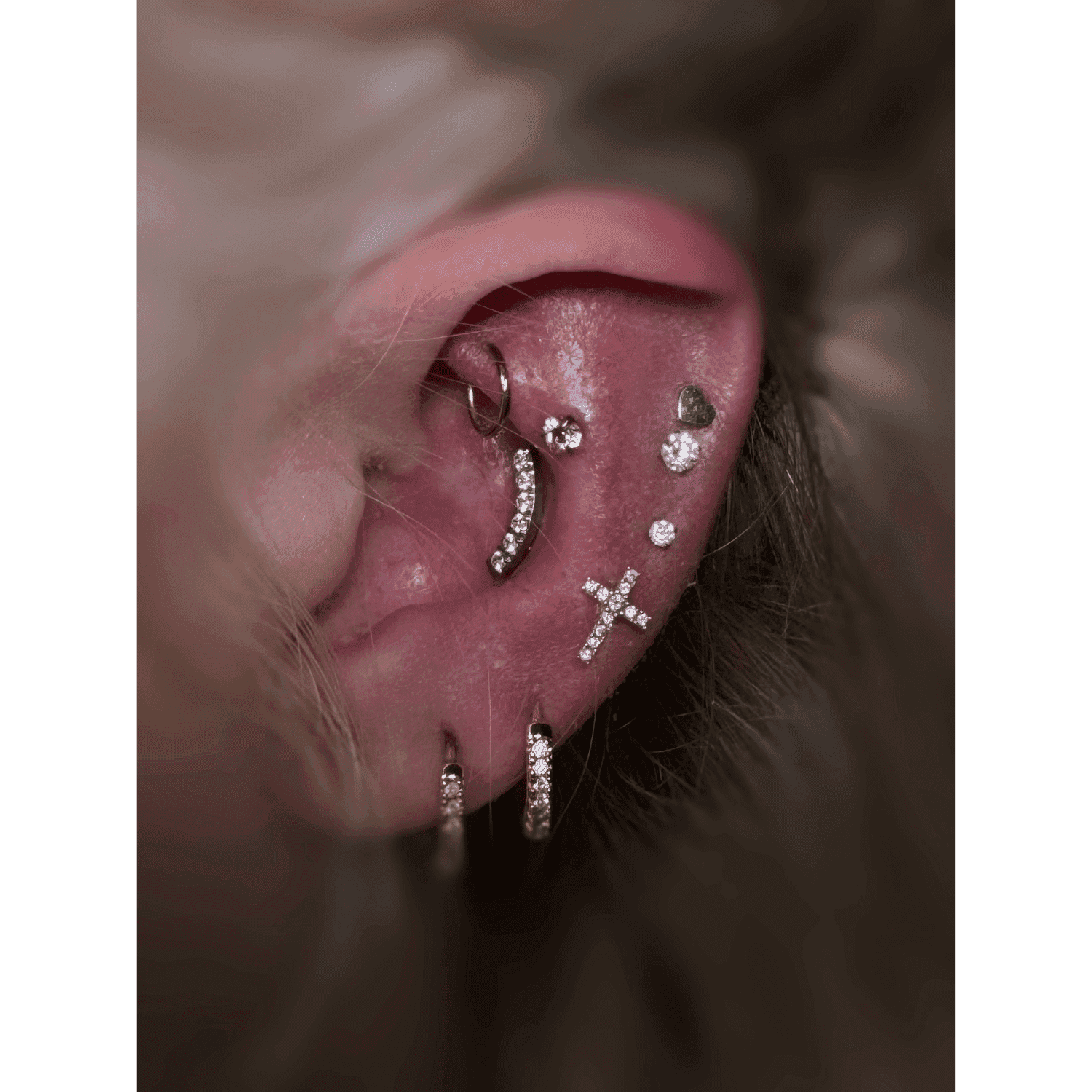 Earlobe and cartilage with multiple earrings and studs, including a cross design.