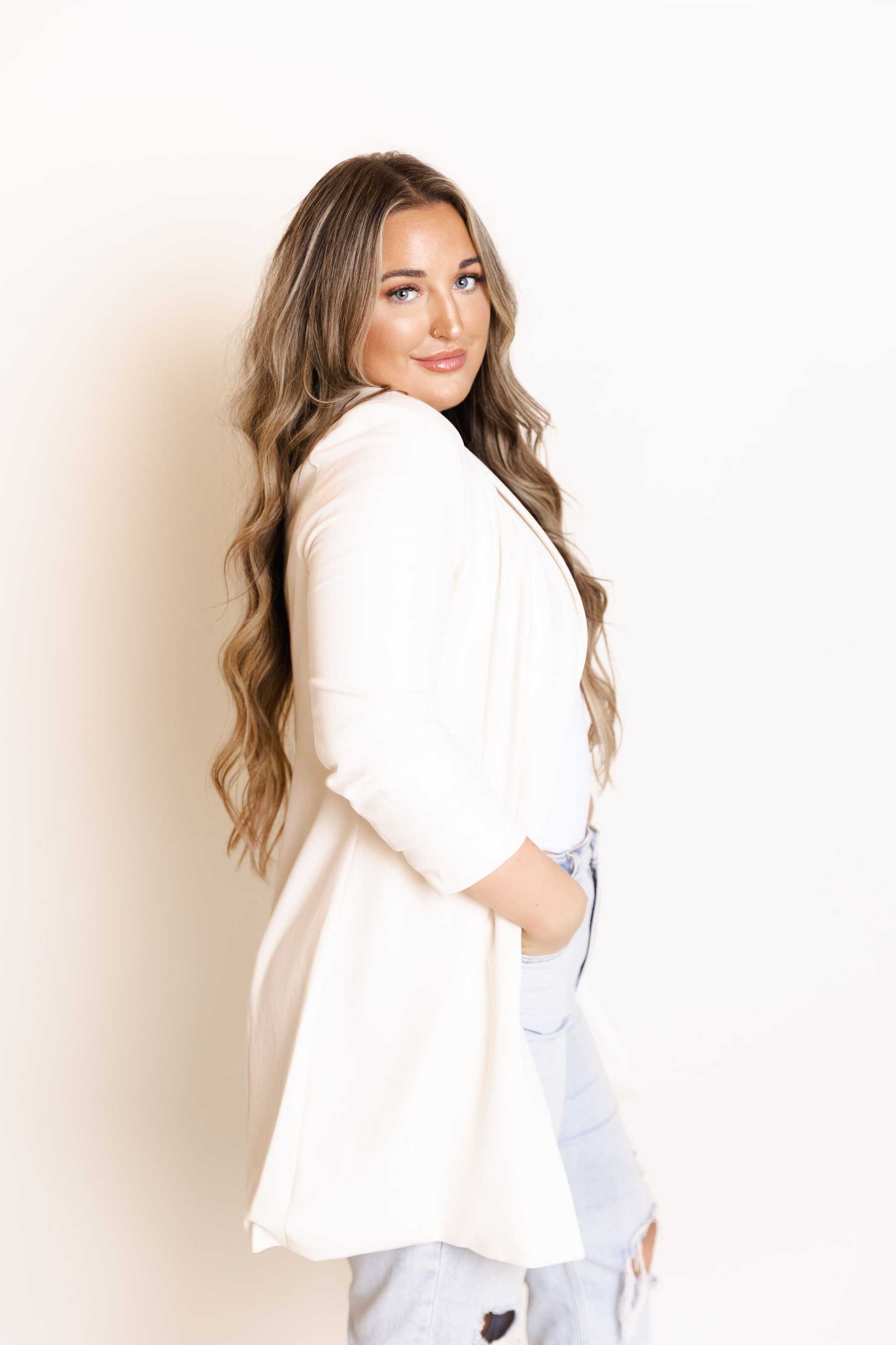 Woman in white blazer posing casually against a white background.